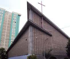 Detalle arquitectónico de la fachada lateral de la iglesia con cruz y fondo urbano