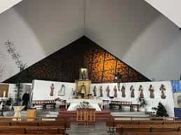 Interior de la iglesia con altar, bancos de madera y decoración religiosa en el fondo