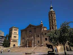 Plaza frontal de la iglesia con escalinata, escultura moderna y cielo azul intenso