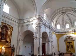 Interior de la nave central con bóvedas decoradas, arcos de medio punto y retablos laterales