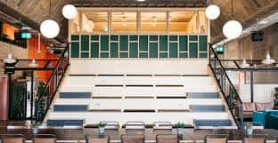 Aula o sala de eventos en PLATF9RM Brighton con gradas, iluminación colgante y diseño acogedor