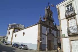 Vista lateral de la iglesia desde la calle, mostrando su fachada blanca y torre con campanas bajo cielo azul