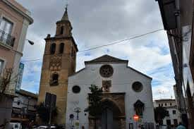 Iglesia Omnium Sanctorum en su entorno urbano con campanario y cielo nublado