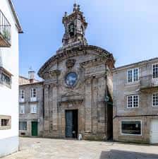 Vista frontal de la iglesia en plaza soleada, mostrando su arquitectura barroca y entorno urbano
