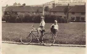 Escena histórica en The Avenue con dos personas y una bicicleta frente a viviendas antiguas