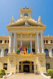 Fachada principal del Ayuntamiento de Málaga con columnas y banderas bajo cielo azul
