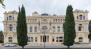 Vista lateral del edificio del Ayuntamiento de Málaga con árboles altos y fachada clásica