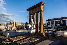 Vista panorámica del cementerio con mausoleos y una estatua central bajo el cielo azul