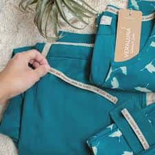 Detalle de ropa de color turquesa con estampado de ballenas y etiqueta de la marca Dendamundi
