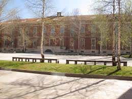 Fachada principal del edificio del Pabellón Universitario en un día soleado con bancos y árboles alrededor