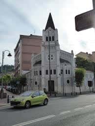 Exterior de la parroquia con coche verde en primer plano, capturando el contexto urbano actual