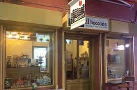 Fachada exterior de Il Boccone con escaparate iluminado y mesas en la acera