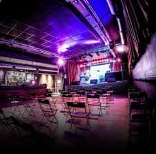 Interior de Sala X con escenario iluminado en tonos púrpuras y butacas dispuestas para evento
