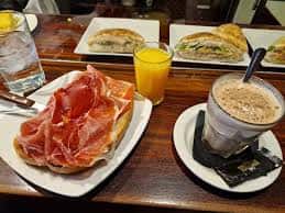 Mesa con desayuno típico español: jamón serrano, tostadas, zumo de naranja y café con leche