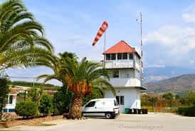 Torre de control del aeródromo con bandera de viento y palmeras
