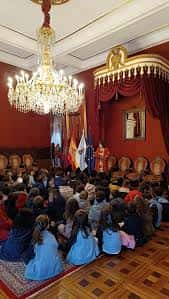 Interior del salón de actos del Concello con decoración clásica, candelabros y audiencia sentada