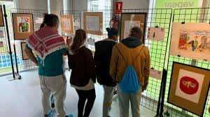 Interior de la sala de exposiciones con obras de arte colgadas y visitantes observando
