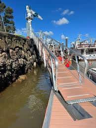 Pasarela de acceso al muelle con barandillas metálicas y embarcaciones al fondo