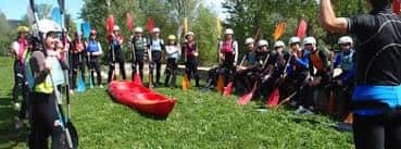 Grupo de participantes en la escuela de piragüismo con kayaks y palas en el césped
