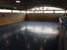 Interior del pabellón deportivo con suelo de parquet y gradas laterales