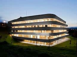 Fachada del Basque Culinary Center iluminada por la noche, destacando sus niveles escalonados y ventanas brillantes