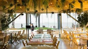 Vista del salón principal con vistas al mar, mesas preparadas para eventos y decoración con plantas colgantes