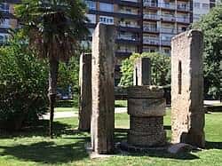 Escultura de piedra y palmera en el parque con edificios al fondo