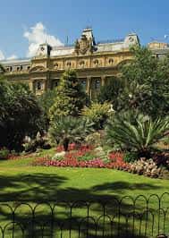 Jardines de la Plaza Gipuzkoa con flores y palmeras frente al edificio histórico