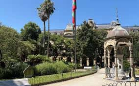 Vista lateral de la Plaza Gipuzkoa con kiosko, bandera vasca y palmeras bajo cielo despejado
