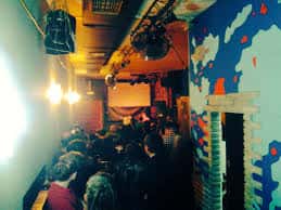 Interior del espacio cultural con público asistiendo a un evento y murales decorativos en las paredes