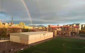 Vista panorámica del campus con campo de fútbol y arcoíris al fondo