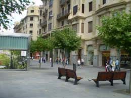 Vista diurna de la Avenida Carlos III en Pamplona con bancos, árboles y peatones