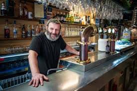 Interior del bar con barra de metal y camarero sonriendo
