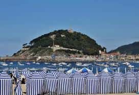 Vista panorámica de la Playa de Ondarreta con el Monte Igueldo al fondo y hamacas a rayas en primer plano