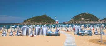 Playa de Ondarreta con hamacas azules y blancas, pasarela central y montañas en el horizonte bajo cielo despejado