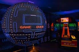 Exposición de videojuegos retro con una esfera de Pac-Man iluminada y máquinas arcade en ambiente oscuro