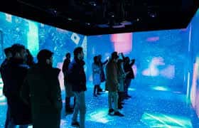Sala inmersiva con proyecciones interactivas en paredes y suelo, con visitantes explorando el espacio