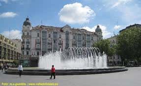 Fuente monumental de la Plaza de Zorrilla con personas caminando alrededor y fachadas clásicas al fondo