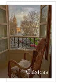Balcón con silla de mimbre y vista a la ciudad y campanario