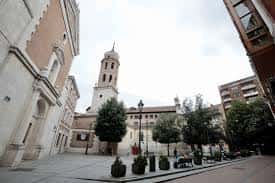 Plaza del Salvador con la torre campanario de la iglesia y árboles en primer plano, vista desde ángulo bajo