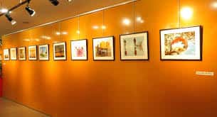 Sala de exposiciones con obras de arte enmarcadas en pared naranja