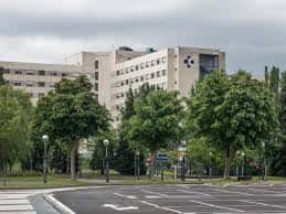 Vista lateral del hospital rodeado de árboles y zona de aparcamiento