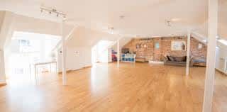 Espacio amplio y luminoso con suelo de madera y paredes de ladrillo, ideal para eventos