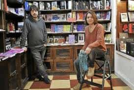 Interior de la librería con estanterías llenas de libros y dos personas en el espacio