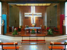 Interior de la iglesia mostrando el altar mayor con cruz luminosa y bancos de madera