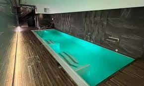 Piscina interior con iluminación azul y revestimiento de madera y piedra