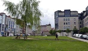 Plaza abierta con árbol de sauce llorón, bancos y personas caminando en un entorno urbano tranquilo