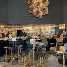 Bar moderno con iluminación dorada, taburetes y decoración floral en la pared