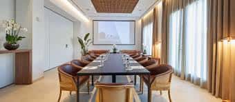 Sala de reuniones elegante con mesa central, sillas de cuero y pantalla de proyección
