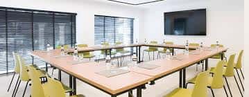 Sala de eventos con disposición en U, sillas amarillas y pantalla de televisión